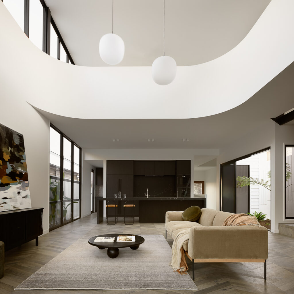 Modern open-plan living room with curved ceiling, neutral furnishings and dark timber herringbone flooring.