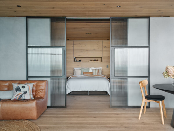 Warm, modern bedroom suite framed by ribbed glass sliding doors, with engineered timber flooring