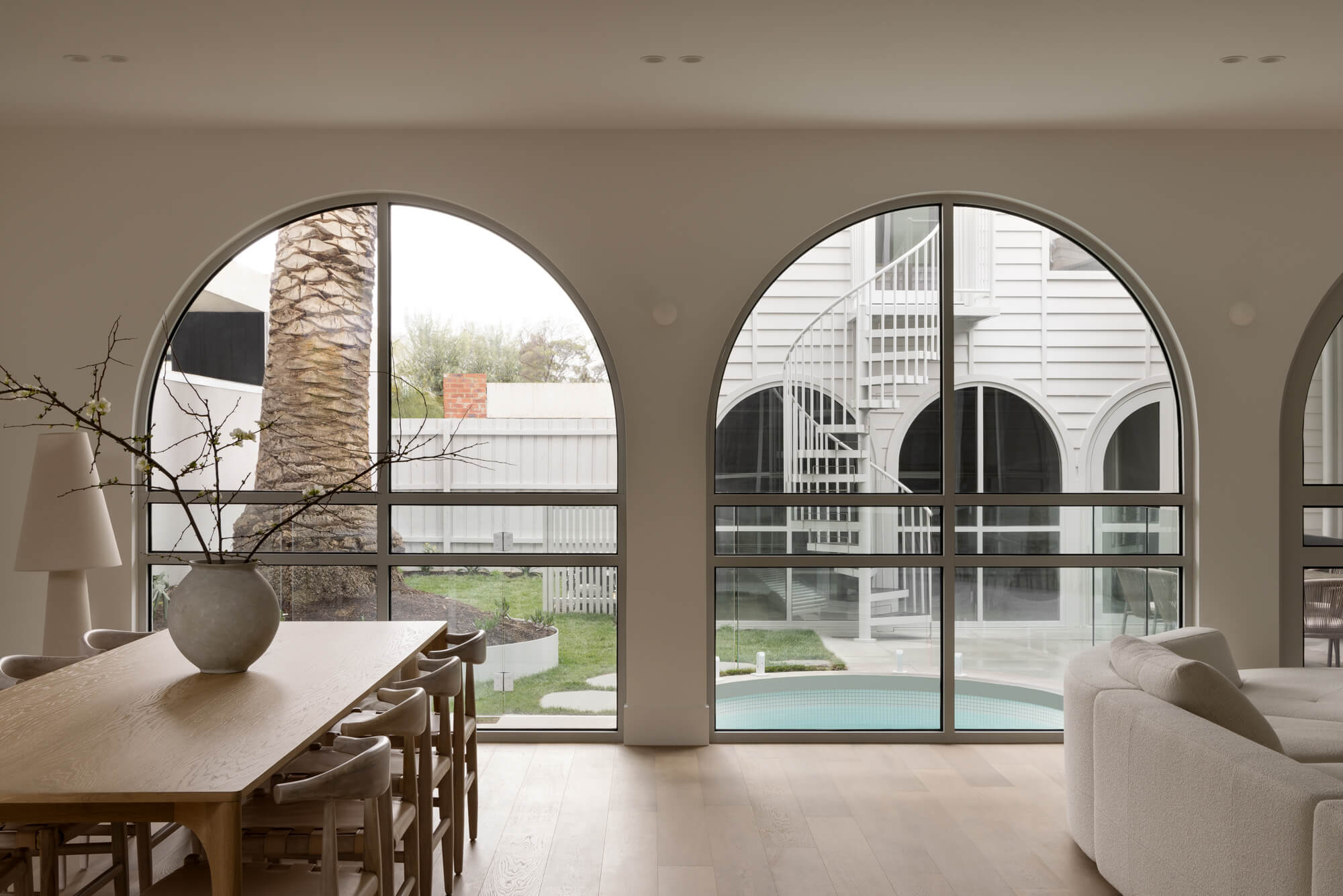 Dining area with wide plank timber flooring, arched black-framed windows, and soft neutral interior styling.