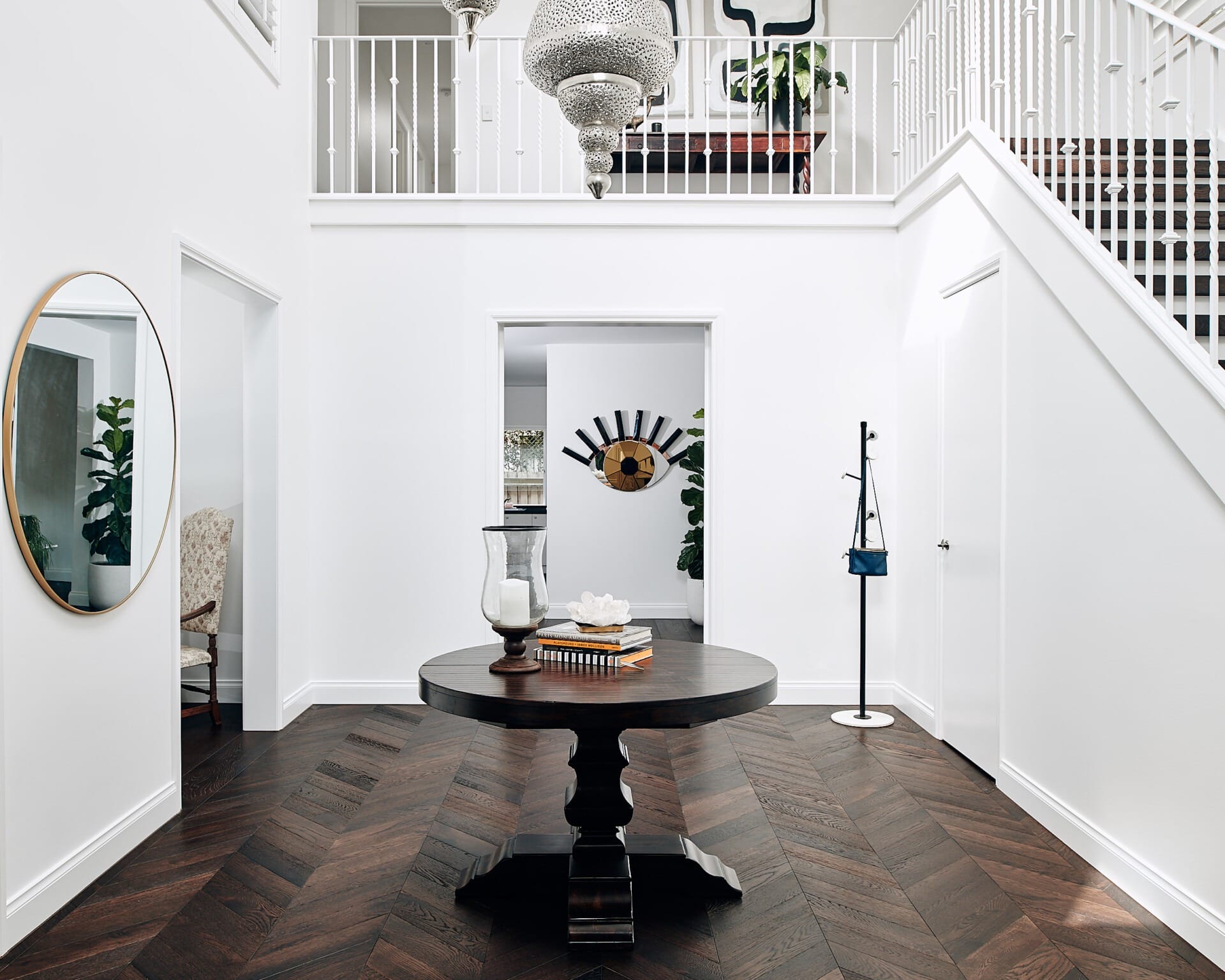 Dark chevron parquetry flooring in grand white foyer with crystal chandelier and sweeping staircase.