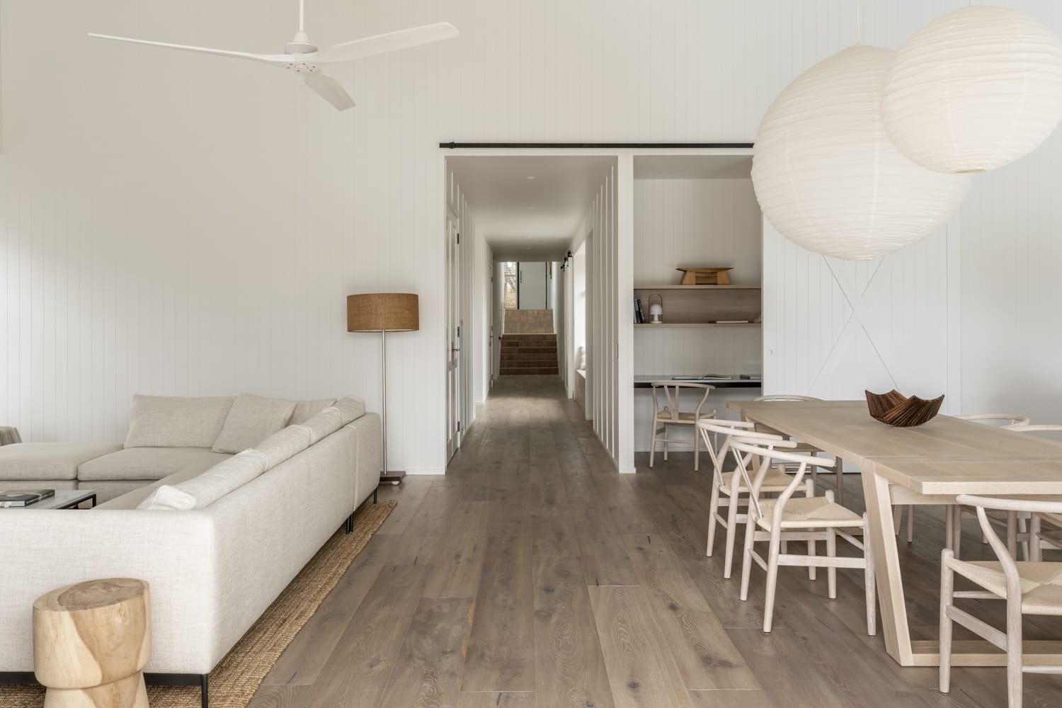 Light-filled Japandi-style living and dining room with natural oak timber flooring, linen sofa, wooden dining table and paper pendant lighting.