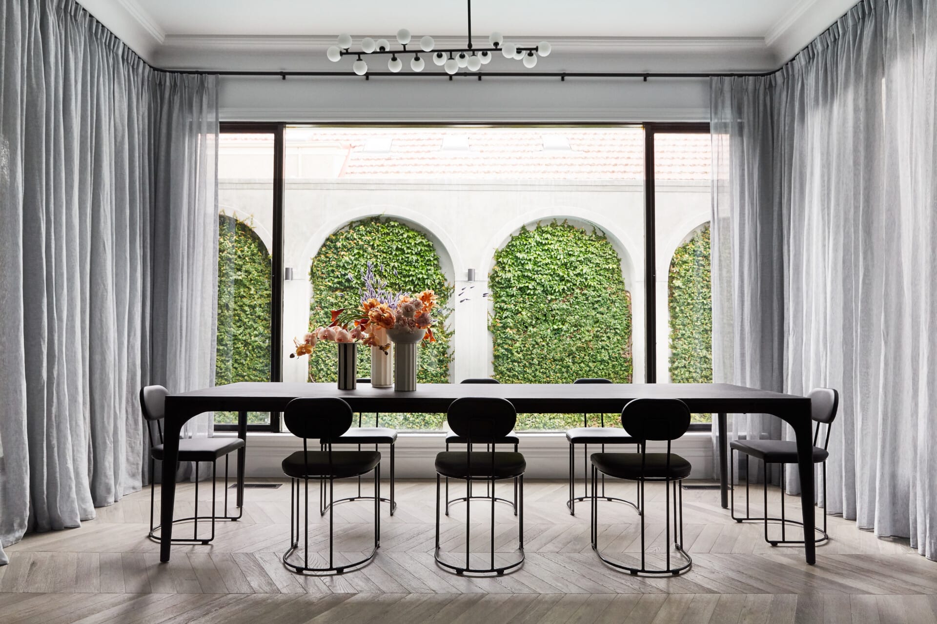 Elegant dining room with large arched windows, long dining table and light oak herringbone timber flooring.