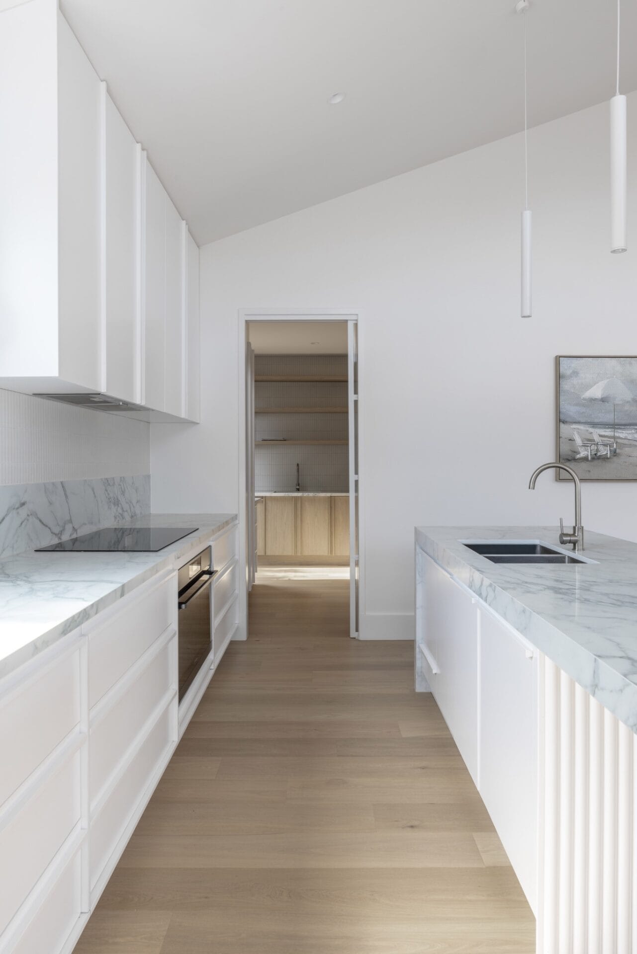 Raked white ceiling drawing daylight down into an all-white kitchen and hallway