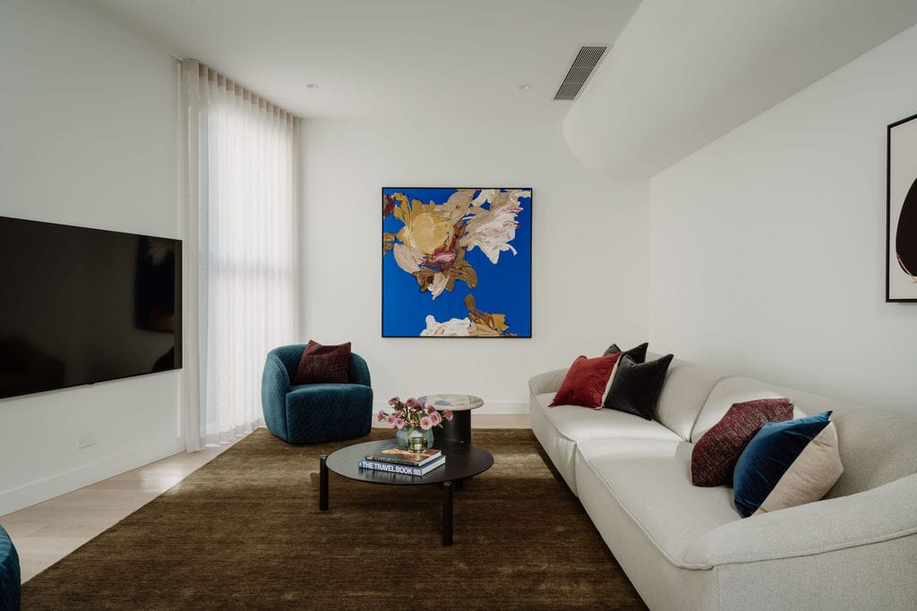 Living room with a pale sofa, blue armchair and framed artwork over timber flooring