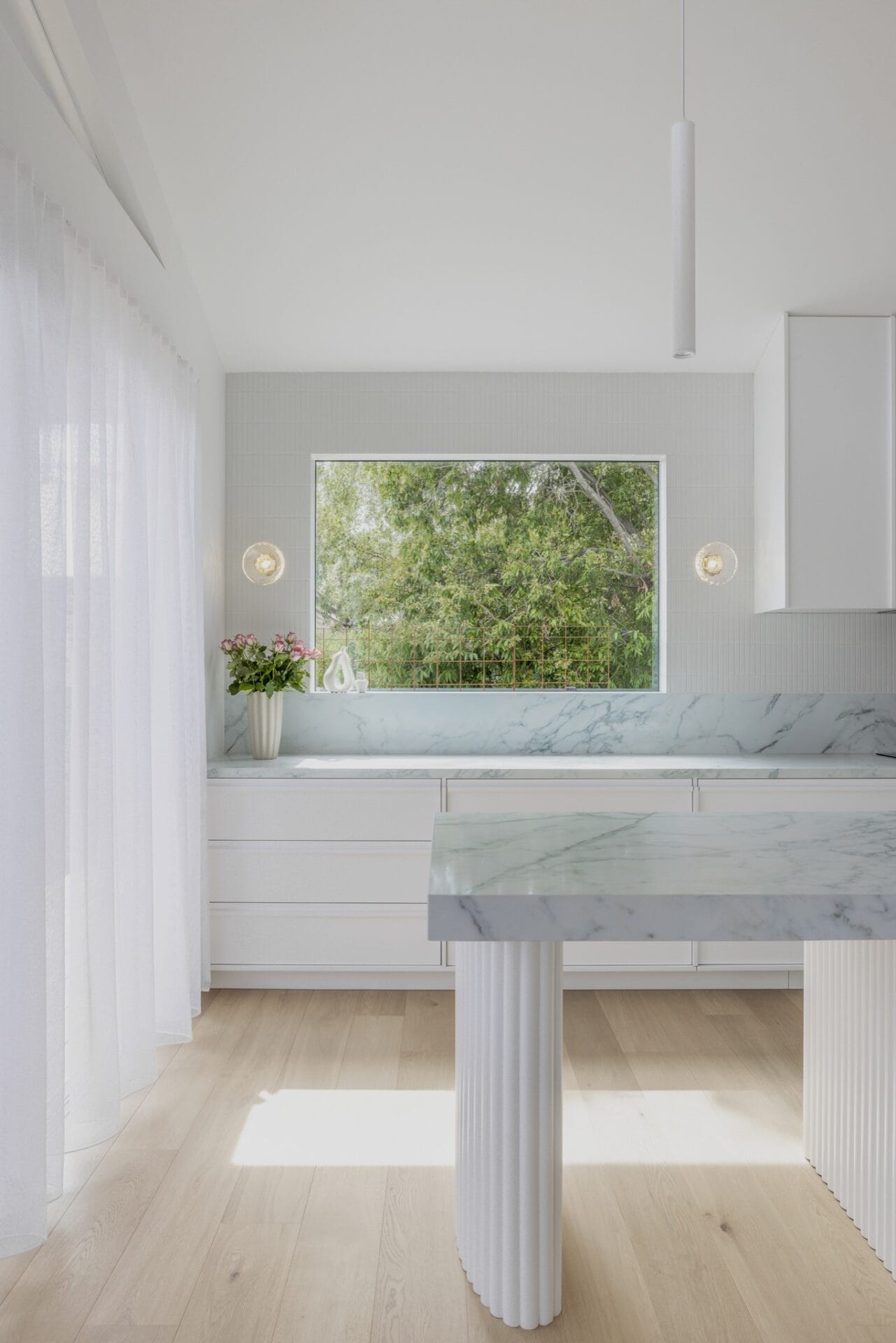 Marble kitchen island with wall sconces and a window framing garden greenery