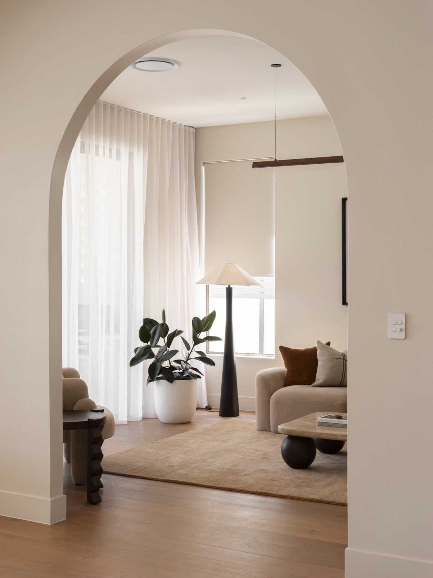 Arched doorway opening into MARÈA's living room with sheer curtains and rust armchair