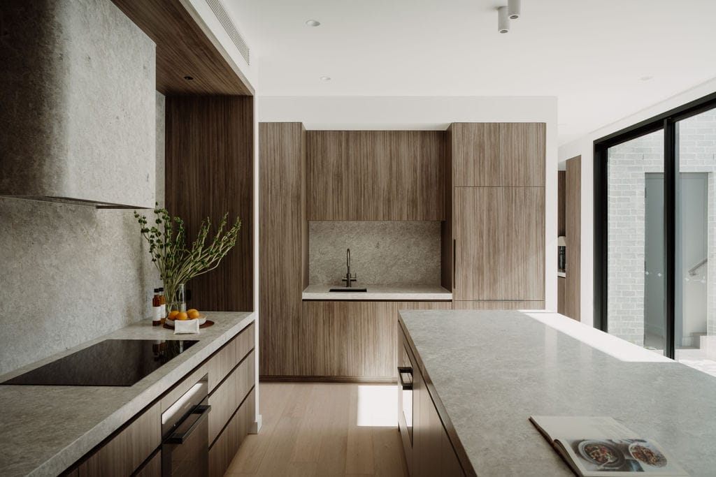 Stone benchtop meeting warm timber joinery, with greenery in the foreground