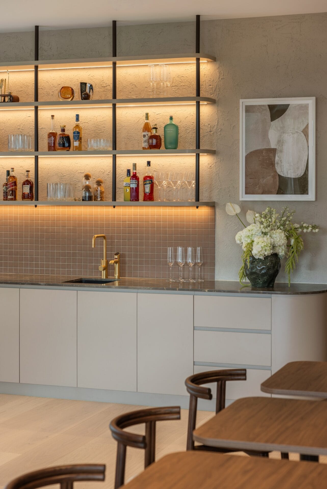 Backlit shelving holding bottles and glassware above a tiled splashback in the office bar