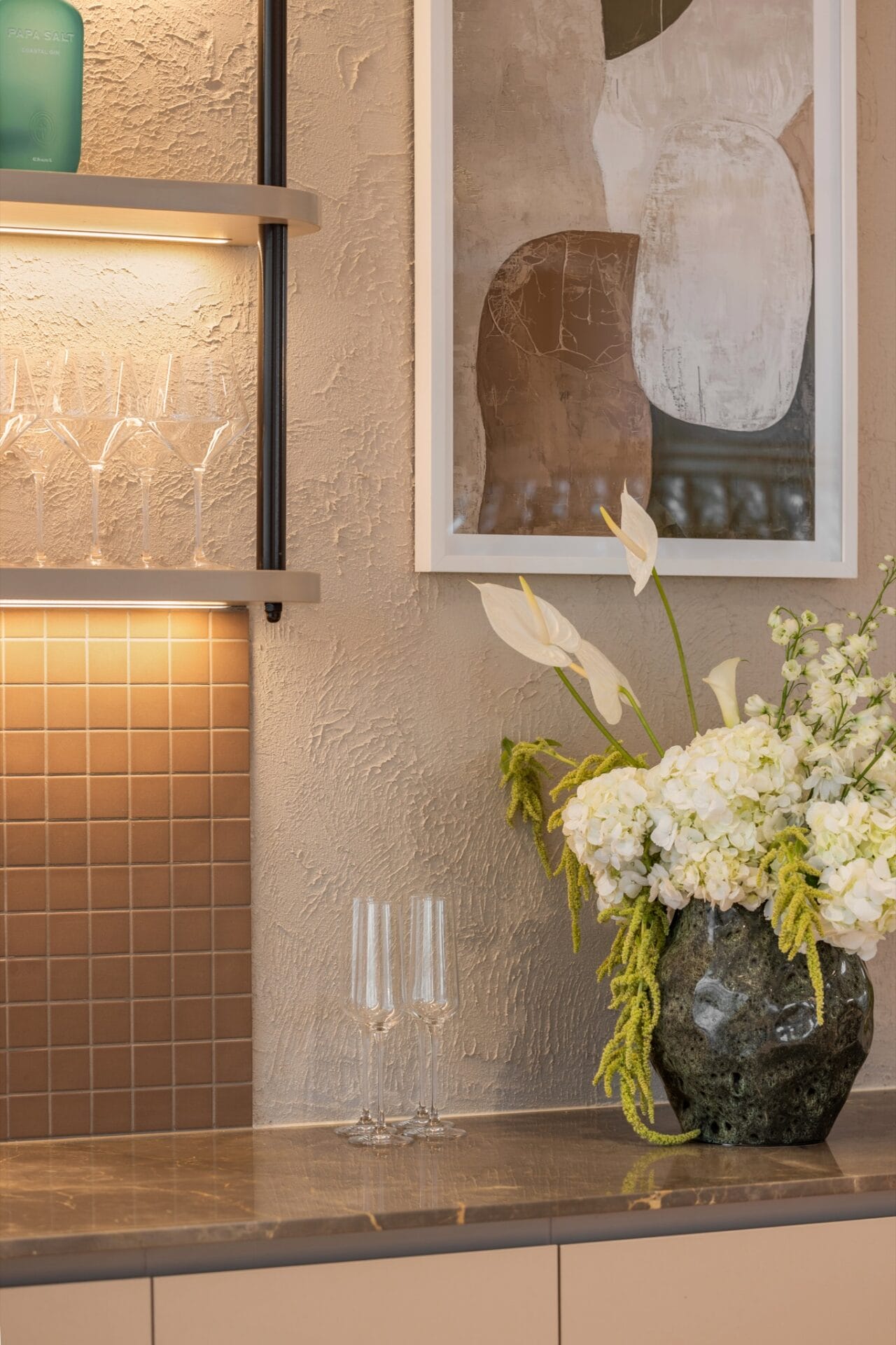 Styling detail with framed artwork, open shelving and fresh flowers against a tiled splashback