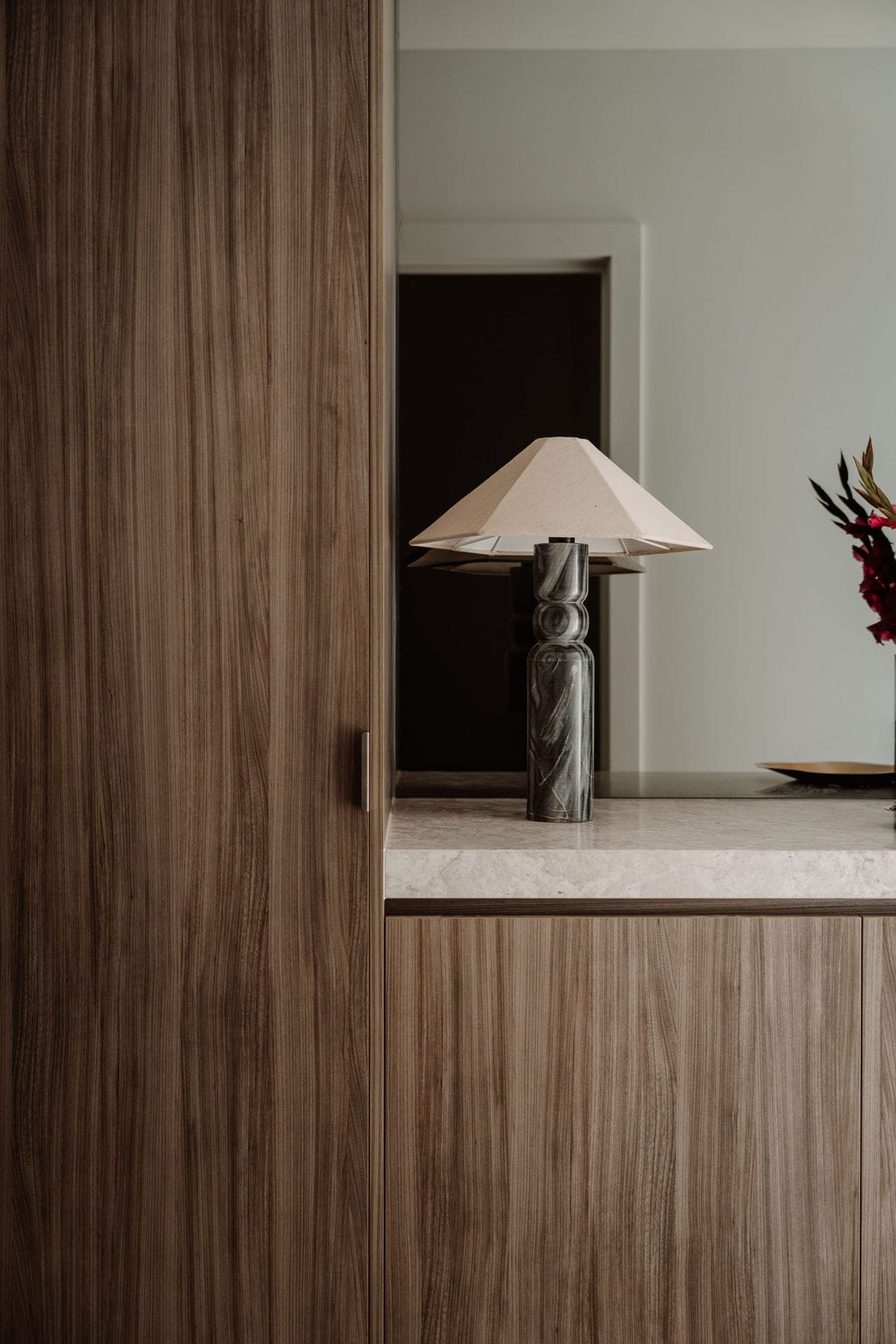 Table lamp beside a timber-lined threshold leading into a bedroom