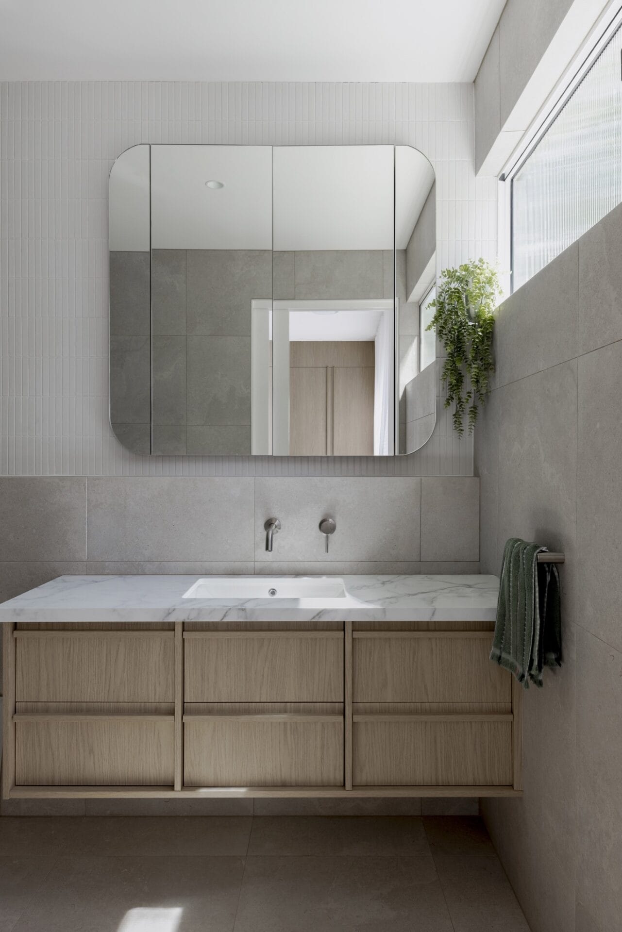 Bathroom mirror reflecting greenery, above soft off-white tiling