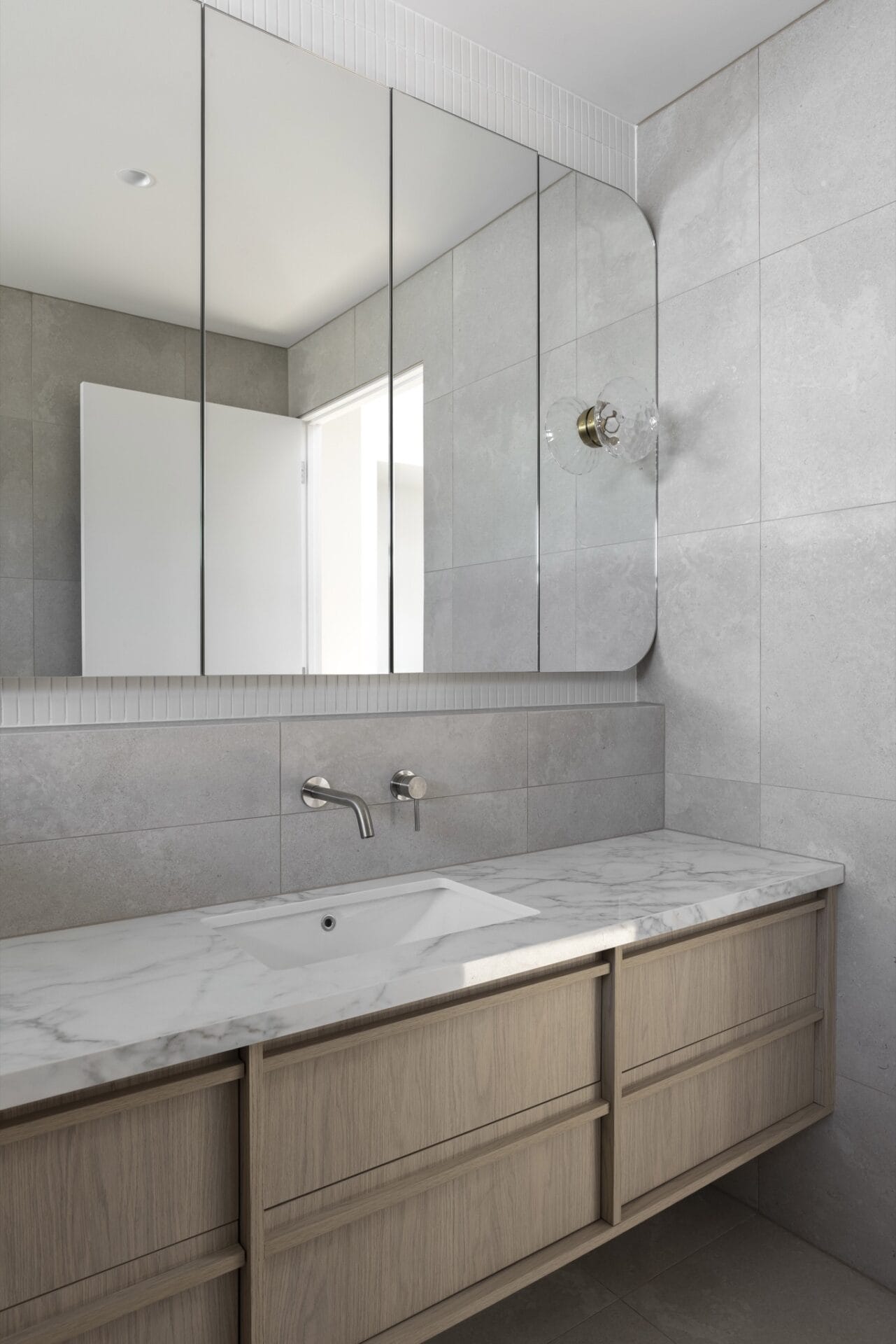 Mirrored cabinetry above a basin, set against tiled walls