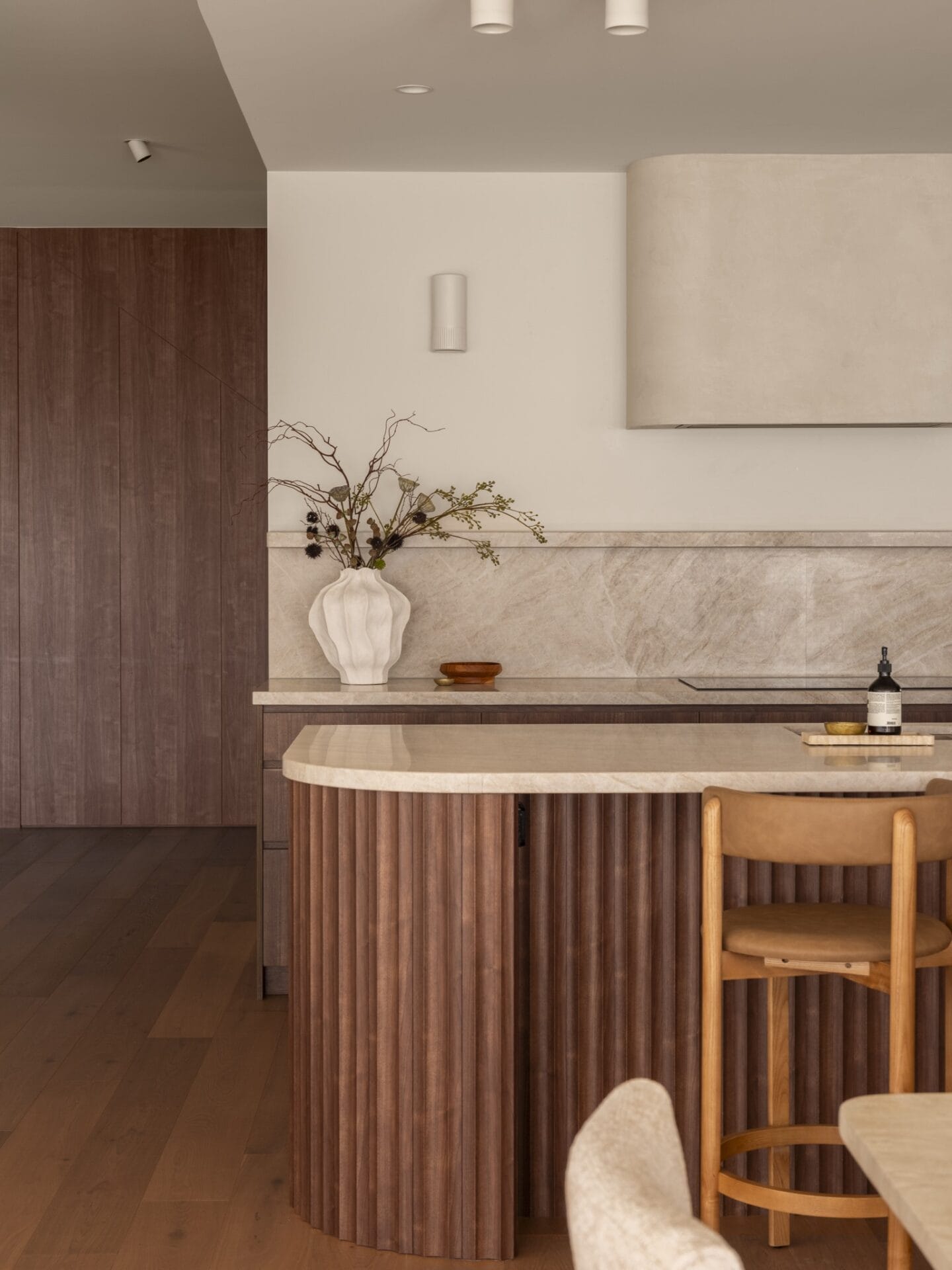 Fluted walnut kitchen island with stone top and timber stools at MARÈA
