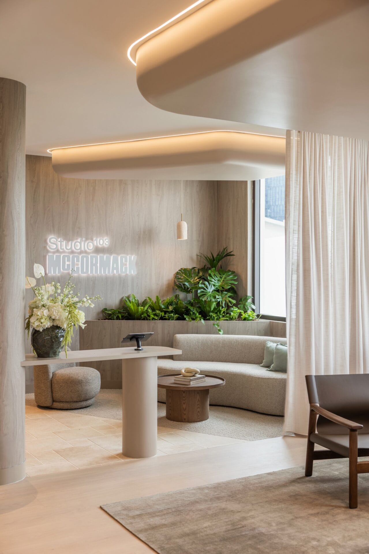 Curved banquette seating and round tables at reception, with planting and timber flooring