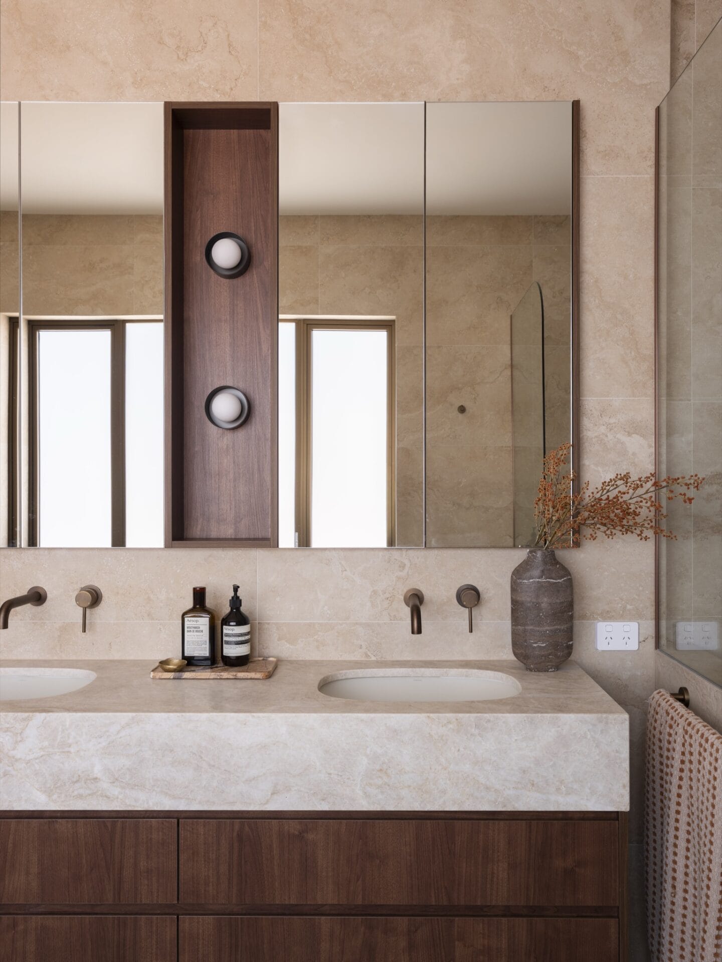 Bathroom vanity at MARÈA with stone basin, walnut cabinet and travertine walls