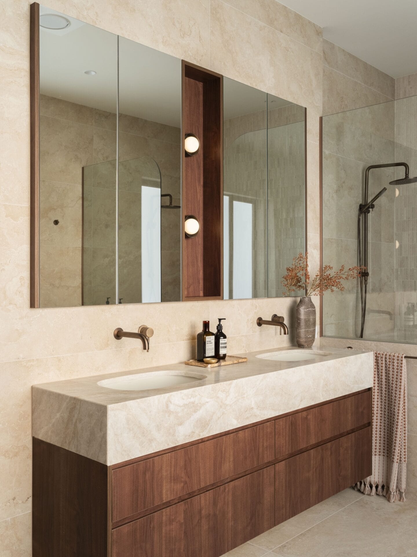 Stone basin and walnut vanity detail with wall sconce at MARÈA