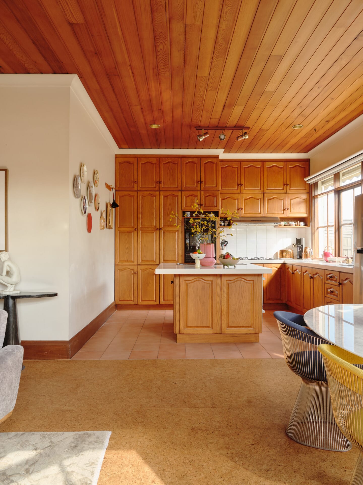 Original oak kitchen with an island bench, terracotta tile meeting Porto cork flooring in the living area beyond.