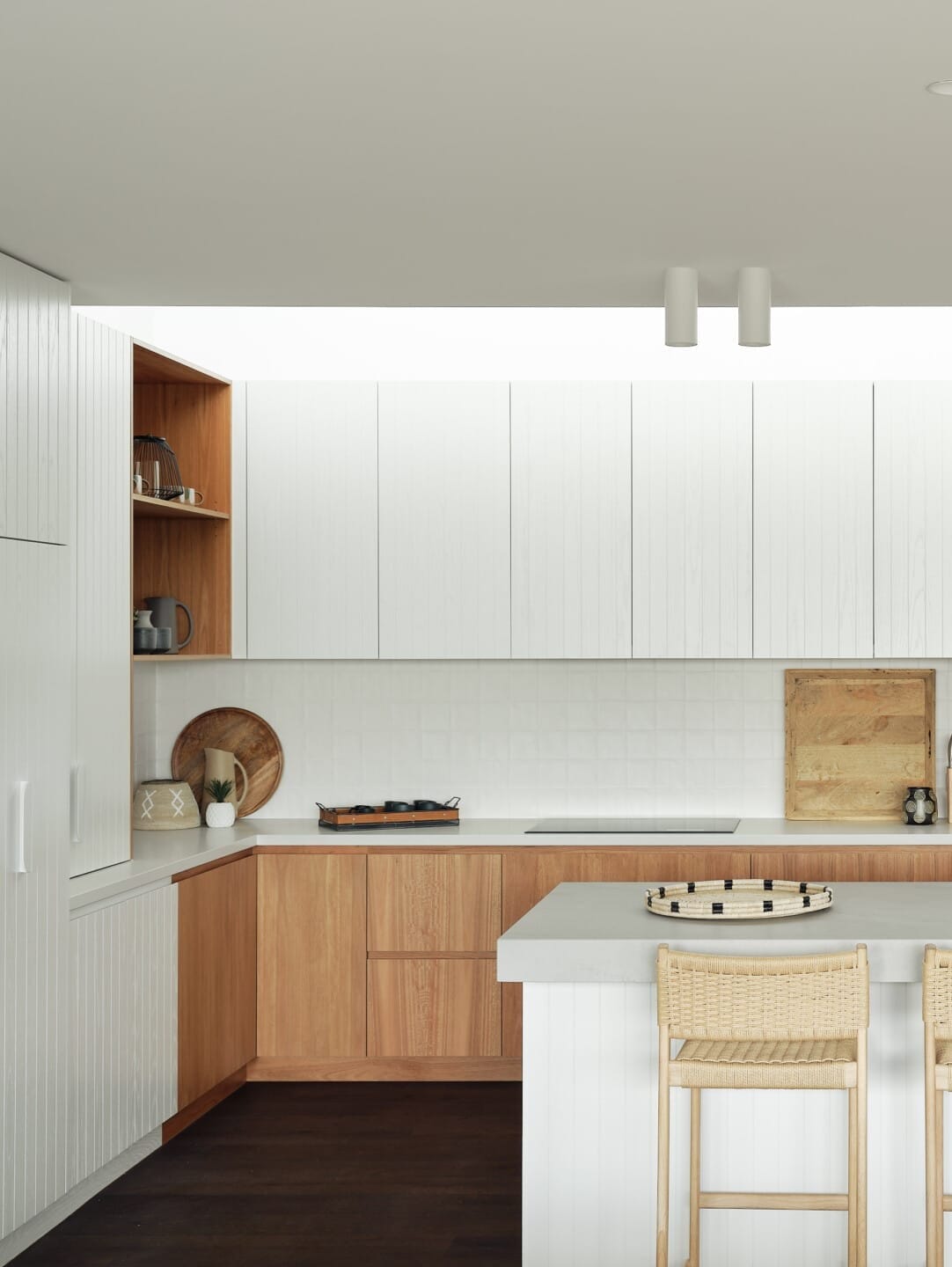 Kitchen with white cabinetry, a timber servery nook, and a curved island bench with woven bar stools, dark timber flooring underfoot.