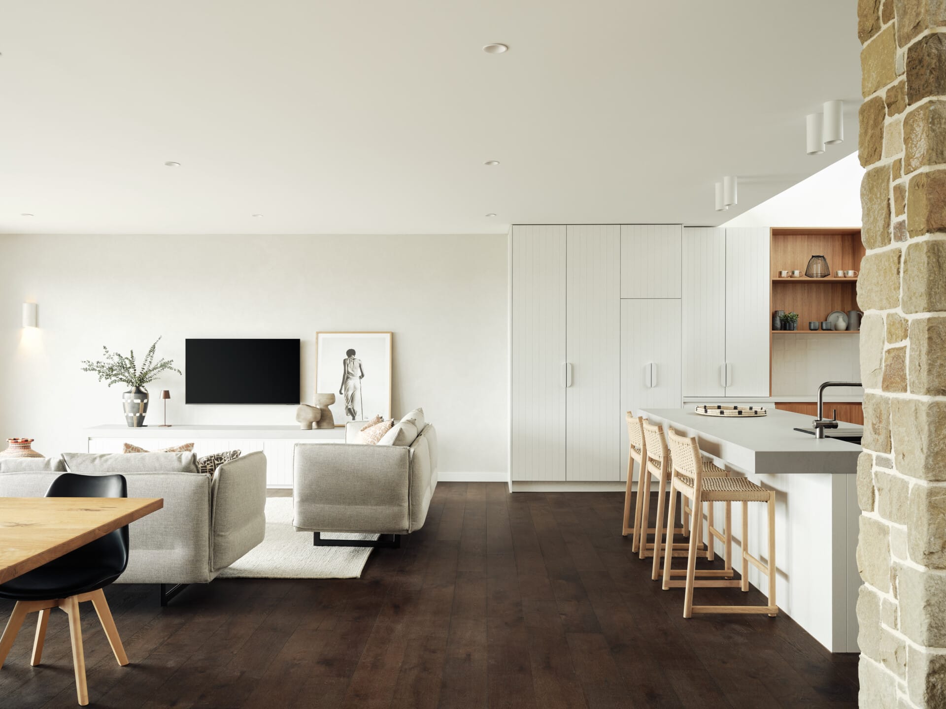 Open-plan living and kitchen area with a stone feature column, white cabinetry and a timber bar with woven stools, Le Cru 190mm timber flooring throughout.