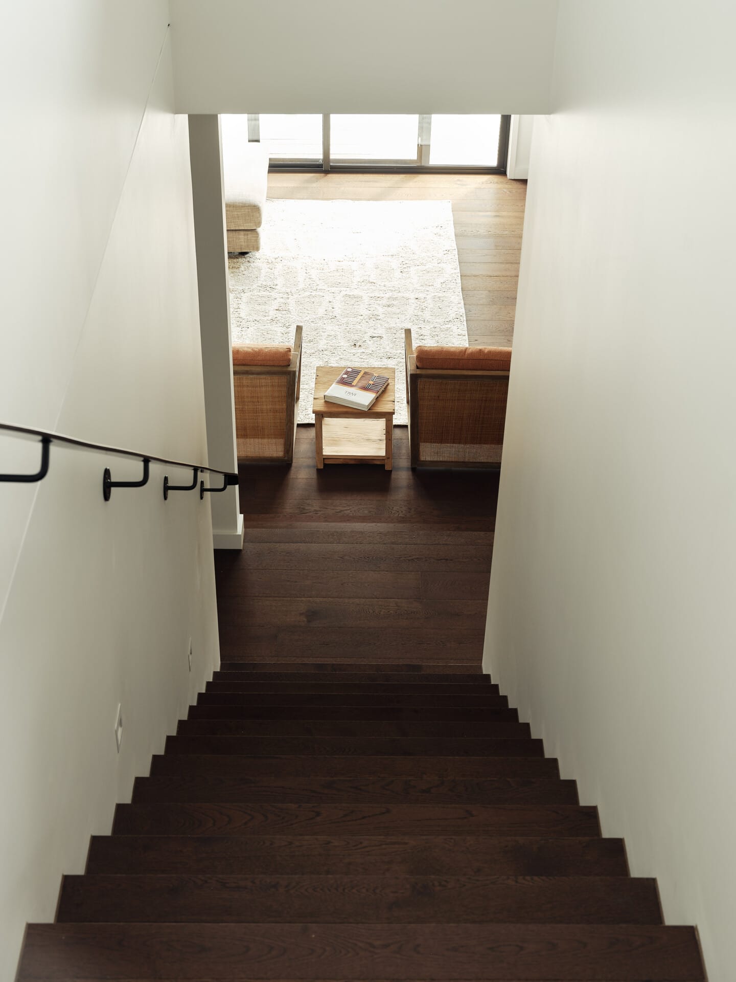 Staircase descending into a lounge with rattan armchairs and a patterned rug, Le Cru 190mm timber flooring throughout.