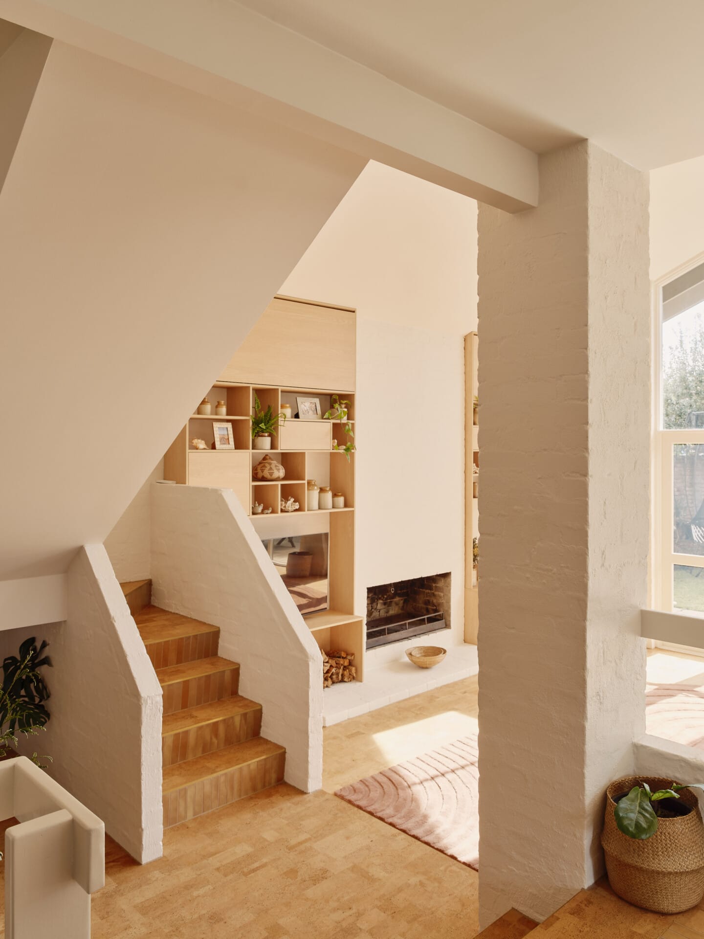 Staircase with built-in shelving and a wood-burning fireplace, a woven rug on Lisbon cork tile flooring, French doors opening to the garden beyond.