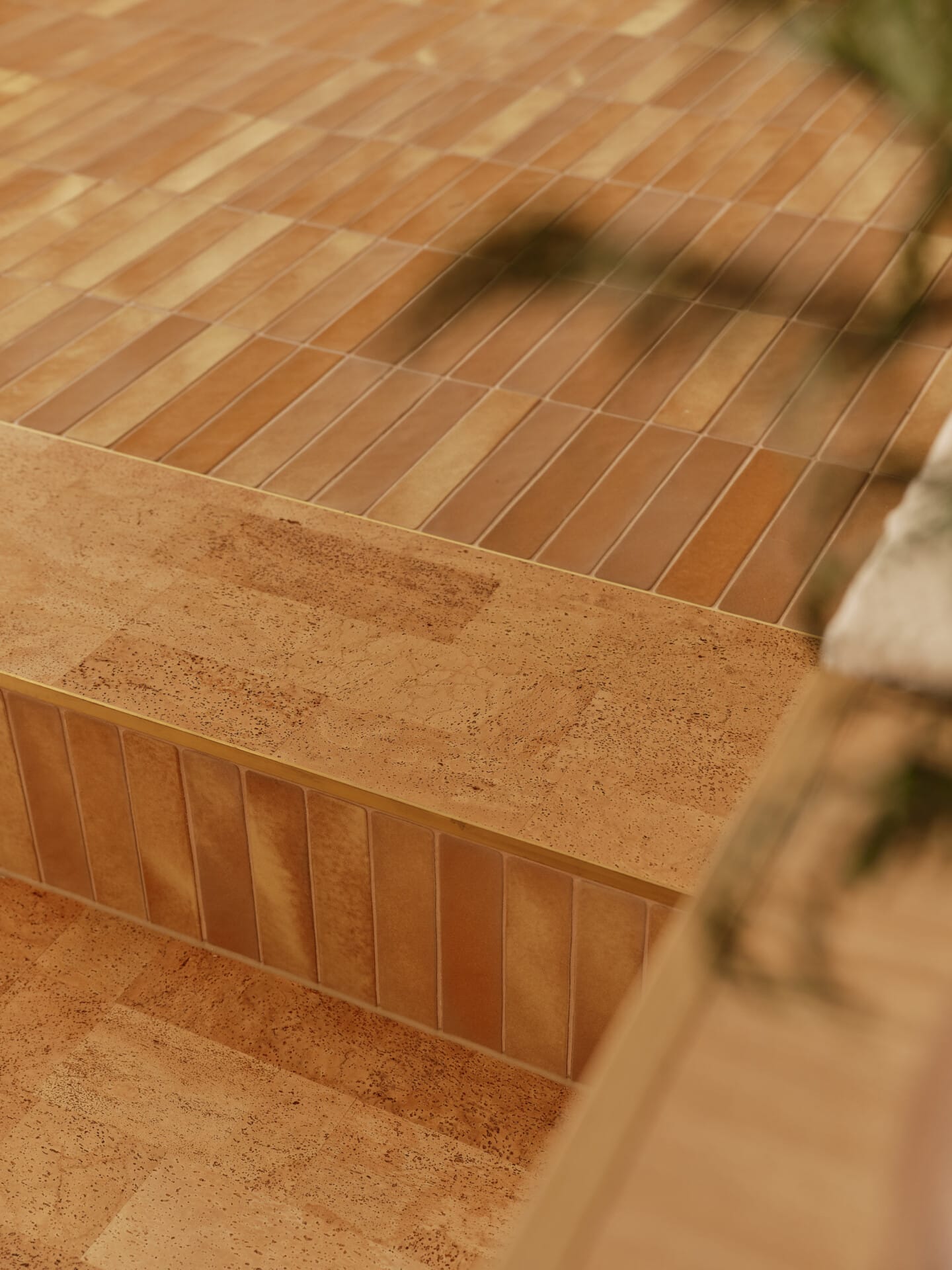 Close-up of a Lisbon cork tile step and landing, with a plant's shadow falling across the floor.