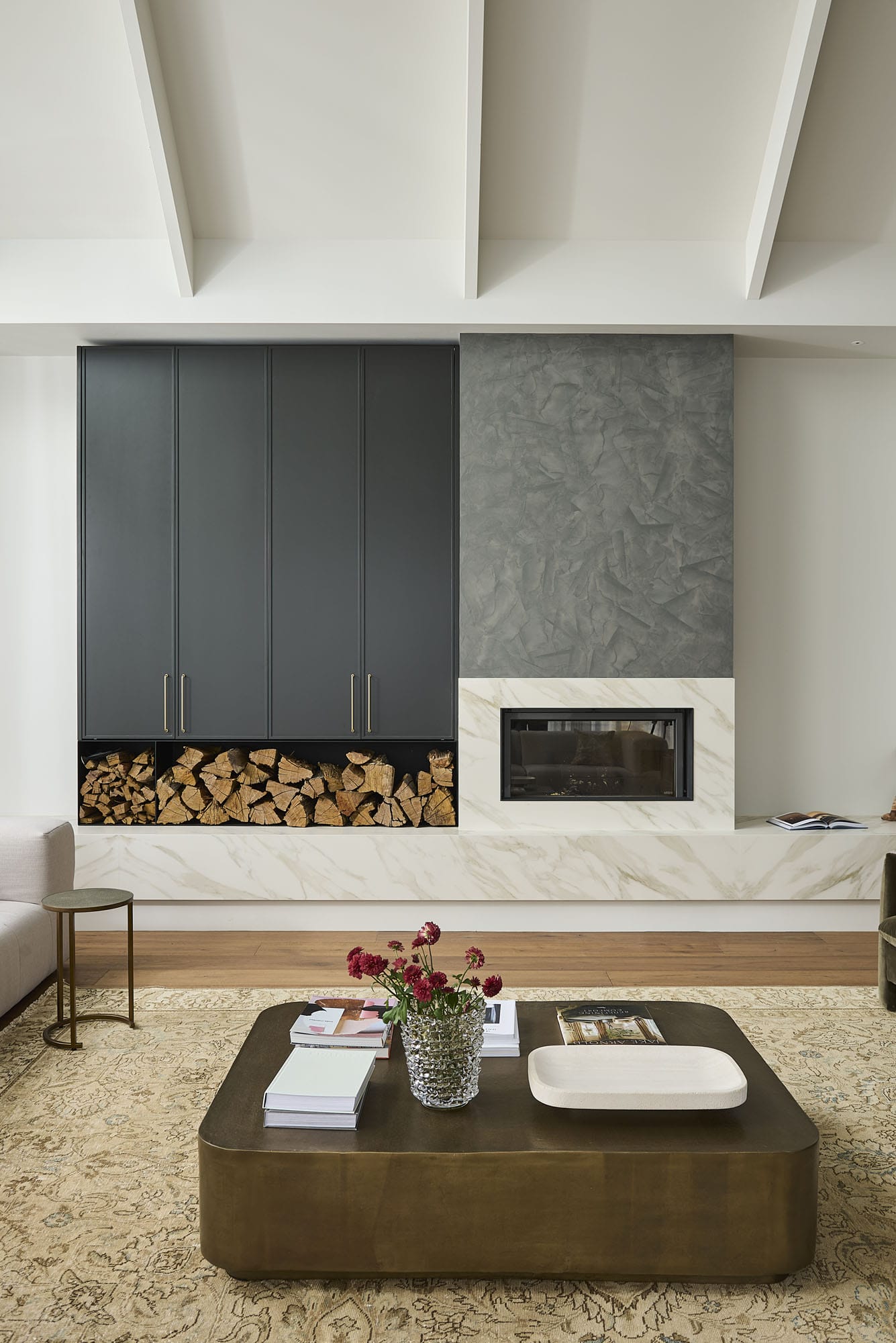 Living room with a stone-clad gas fireplace, built-in firewood storage, and a leather coffee table on a rug, Diamond Bay timber flooring at Riverstone House.