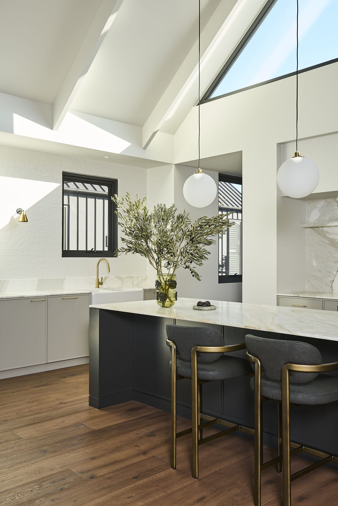 Kitchen island with marble benchtop, charcoal cabinetry, and brass barstools, Diamond Bay timber flooring underfoot at Riverstone House.