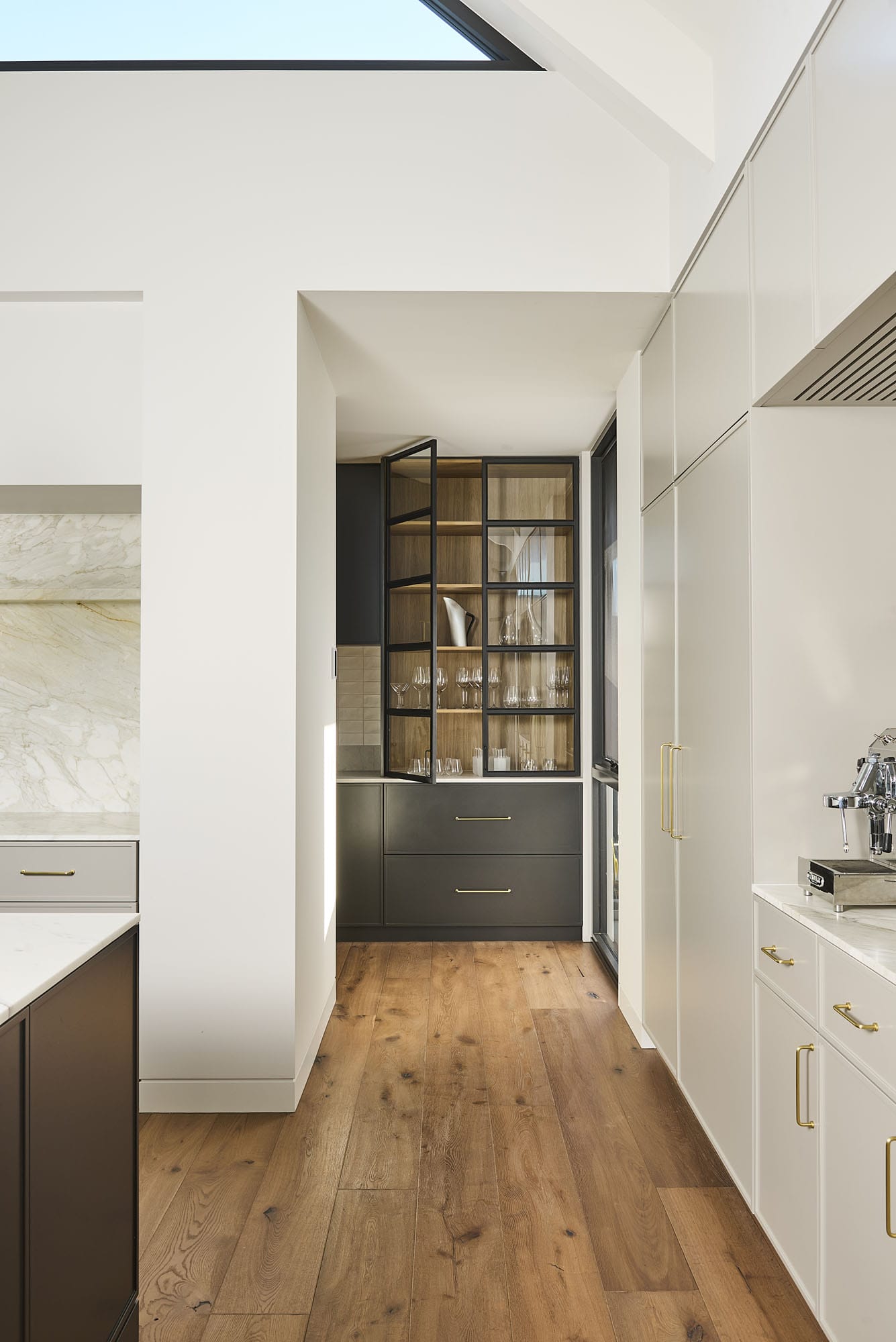 Butler's pantry with glass-fronted cabinetry, brass hardware, and Diamond Bay timber flooring leading through from the kitchen at Riverstone House.