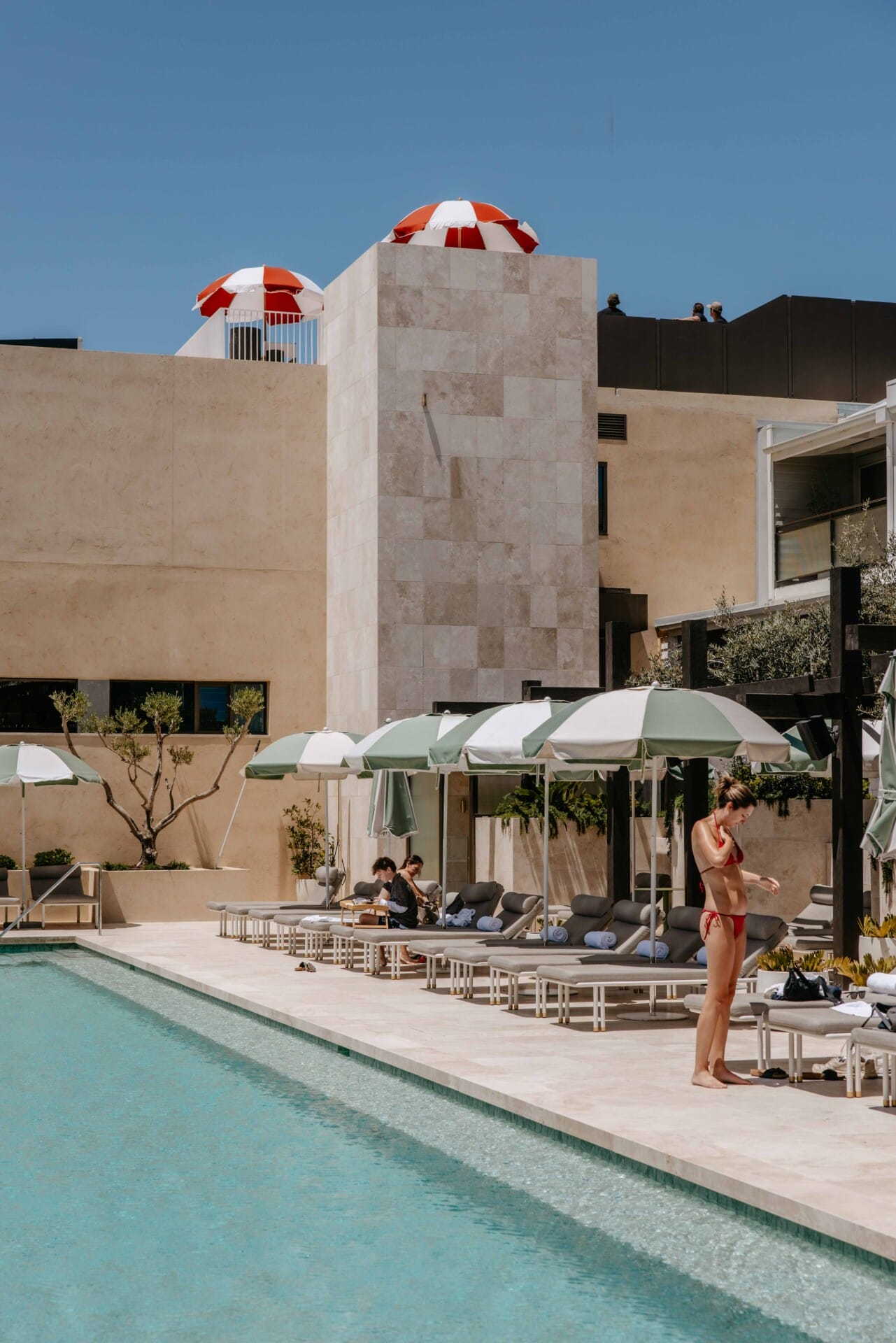 Hotel Sorrento pool deck with striped umbrellas, sun loungers, and the travertine-clad exterior under clear skies.