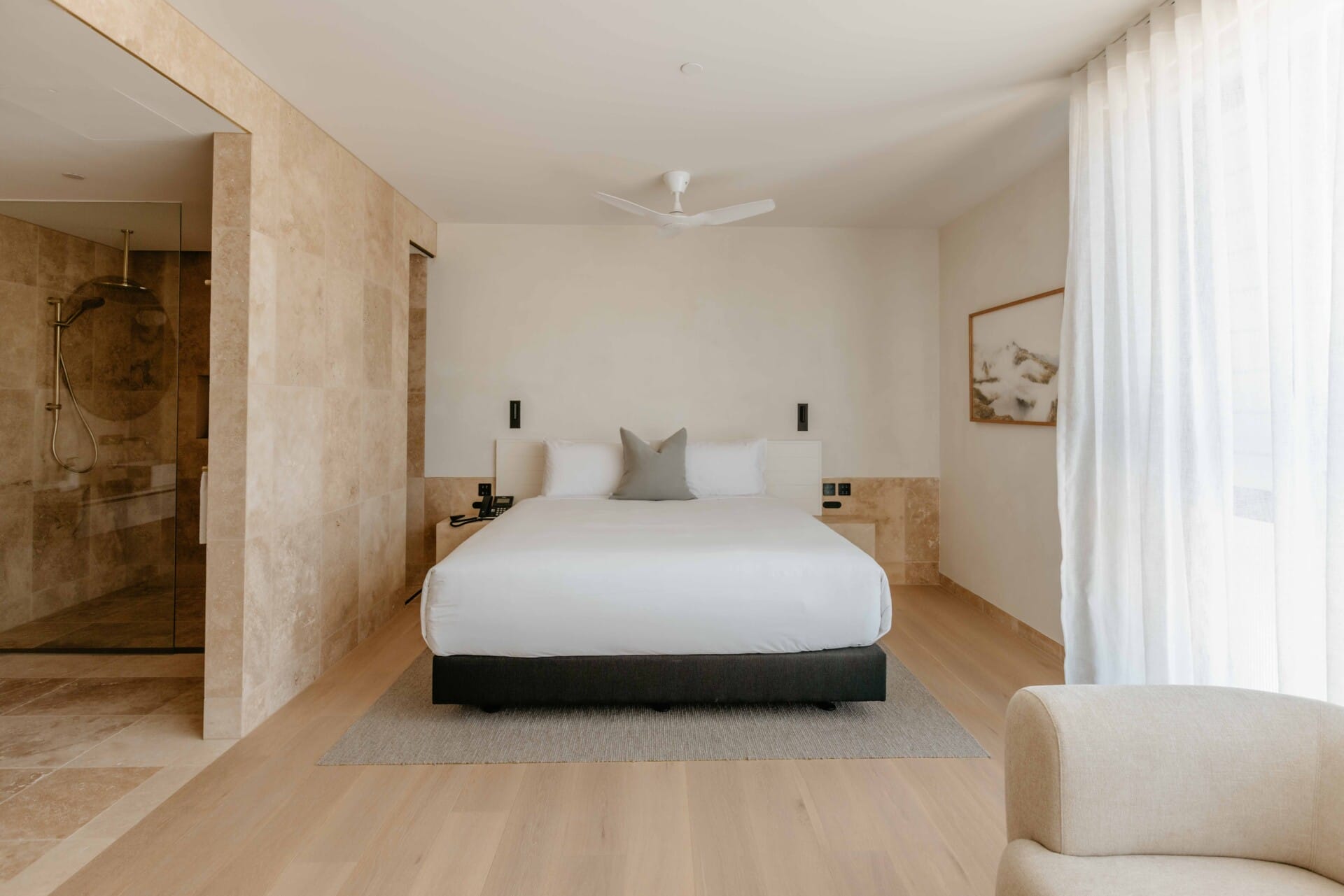 Hotel Sorrento guest suite bedroom floored in Kustom Timber Habitat Calypso 190mm engineered oak, with a king bed, sheer curtains, and a travertine-clad ensuite.
