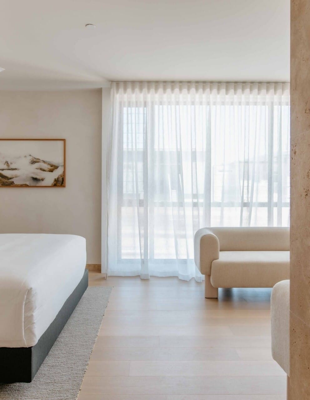 Hotel Sorrento guest suite bedroom floored in Kustom Timber Habitat Calypso 190mm engineered oak, with sheer curtains opening onto a coastal view and a bouclé armchair.