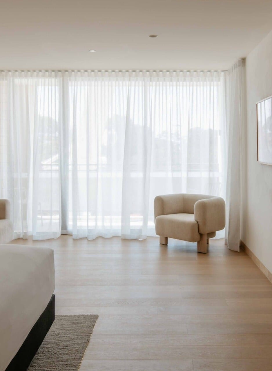 Hotel Sorrento guest suite floored in Kustom Timber Habitat Calypso 190mm engineered oak, with a sheer-curtained window and a bouclé armchair overlooking the coastline.