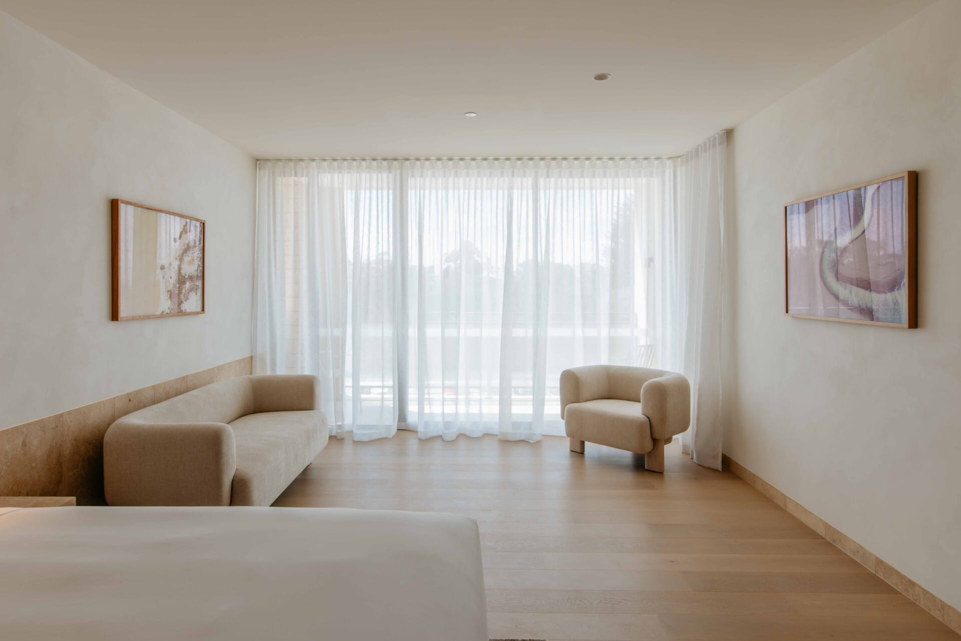 Hotel Sorrento guest suite floored in Kustom Timber Habitat Calypso 190mm engineered oak, with a bouclé sofa and armchair framed by sheer curtains and coastal light.