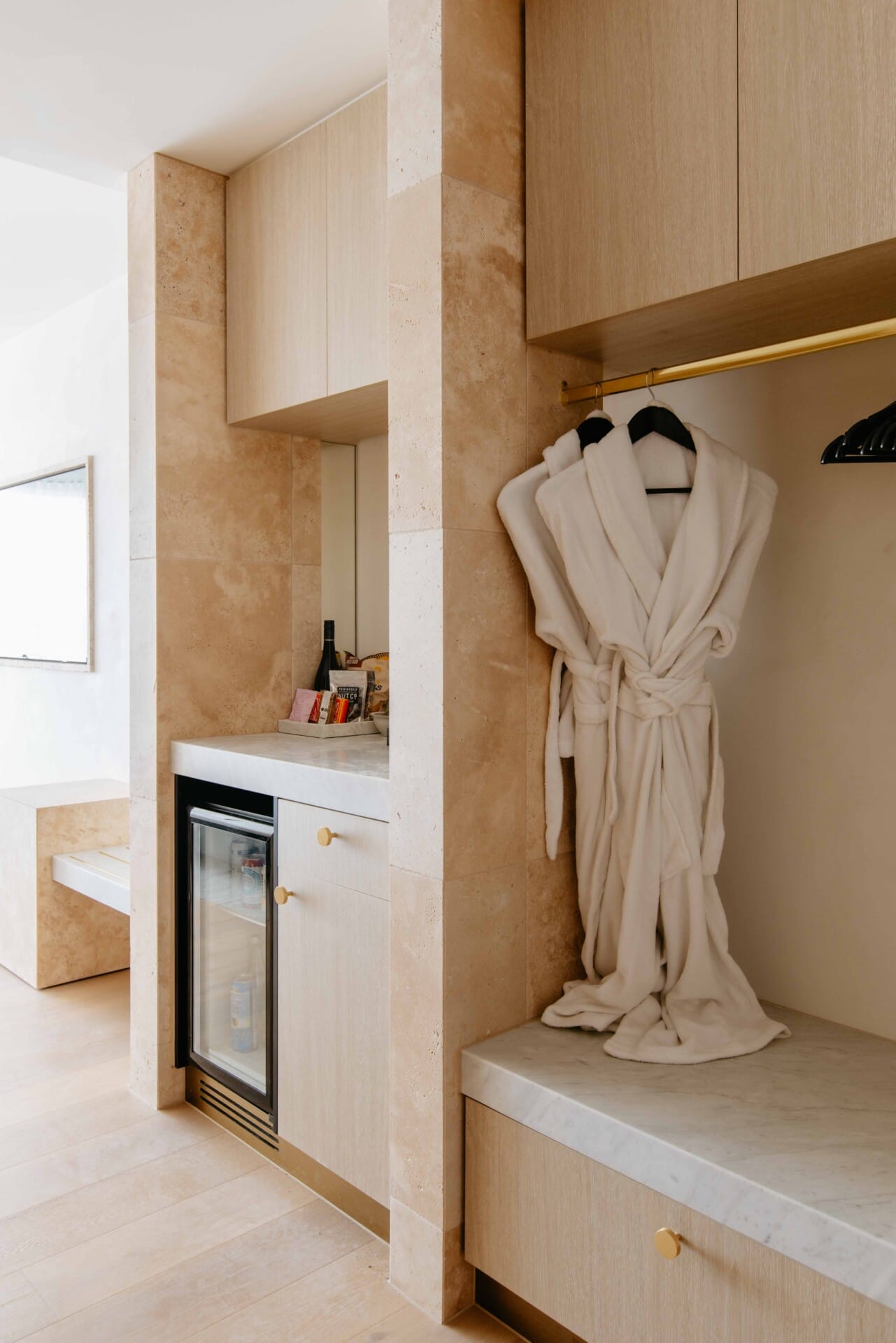 Hotel Sorrento guest suite wardrobe nook with a mini bar, robes, and travertine-clad joinery.