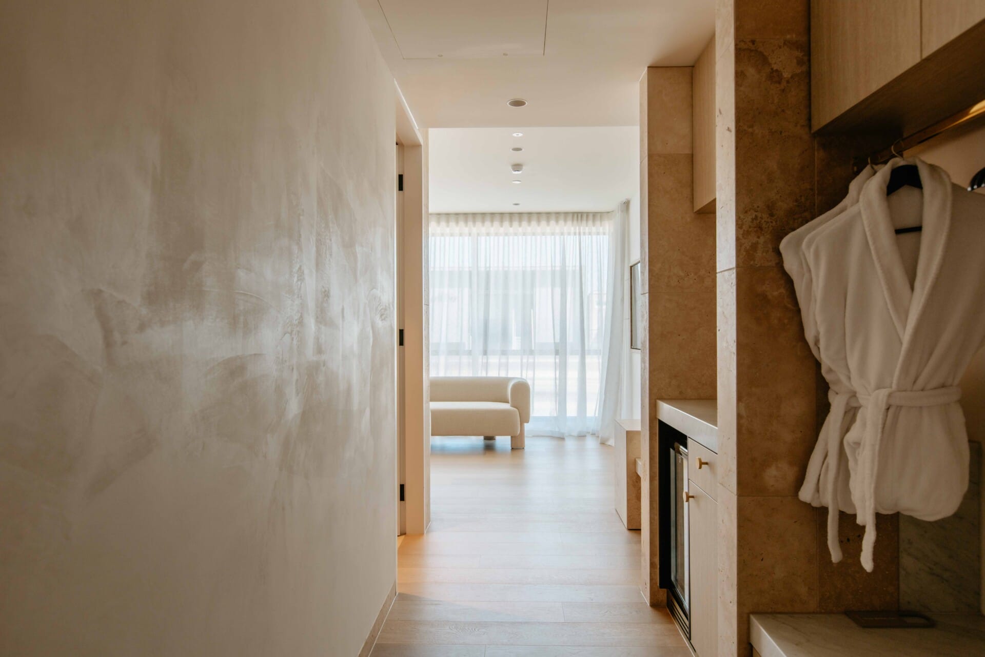 Hotel Sorrento guest suite hallway floored in Kustom Timber Habitat Calypso 190mm engineered oak, leading to a sitting area with sheer curtains and coastal light.